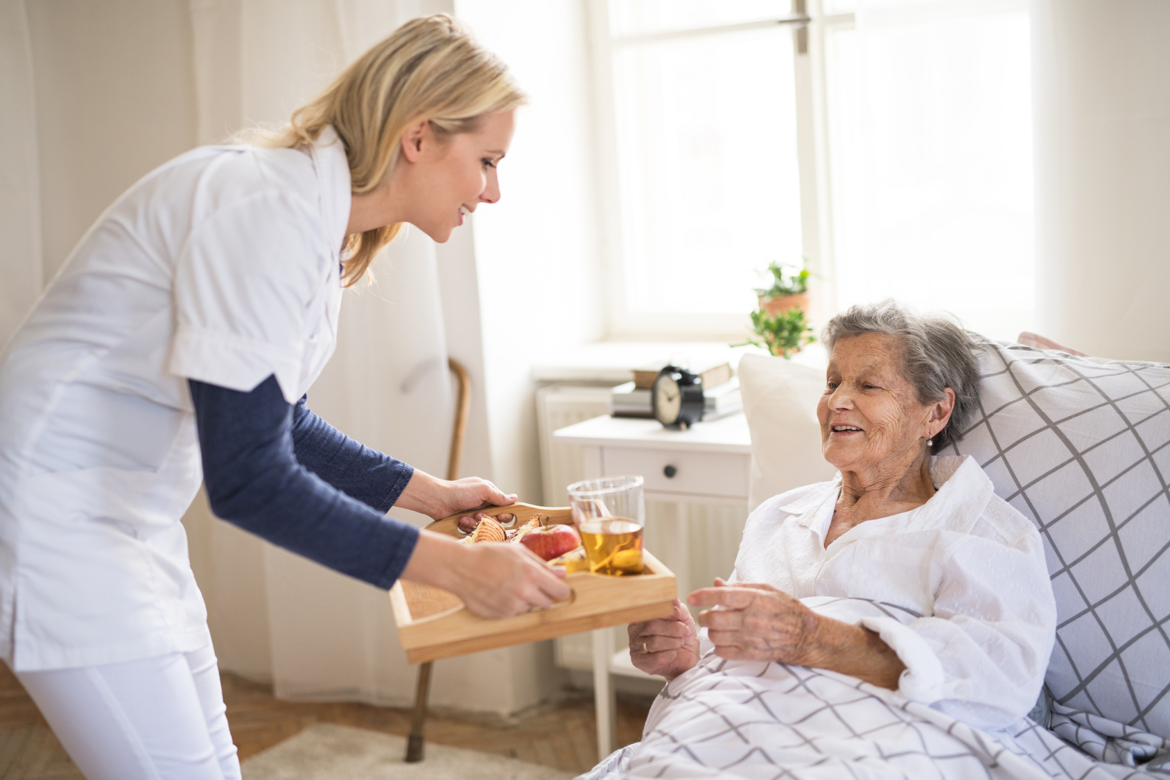 A home care nurse bringing breakfast to an older woman resting in bed