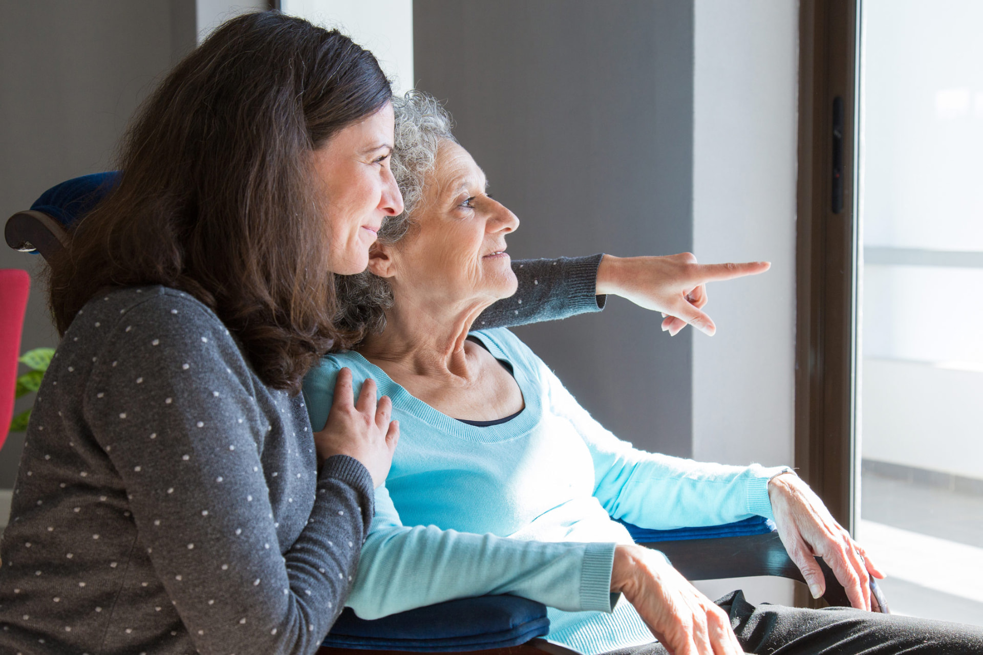 An adult daughter sitting beside her mother, both looking out a window